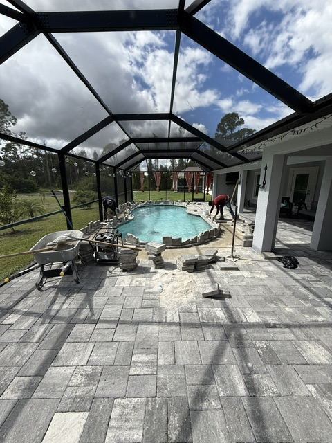 Paver installation around a pool area with workers laying stones, showcasing a completed paver surface in a residential setting in Southwest Florida.