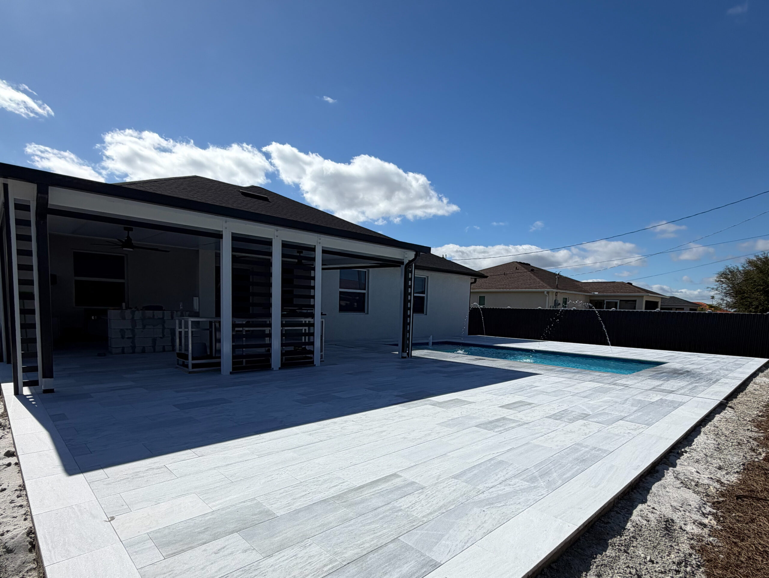 1 Modern outdoor patio with elegant paver flooring, featuring a pool with water fountains, under a clear blue sky, showcasing quality paver installation by Elite Pavers Solutions.