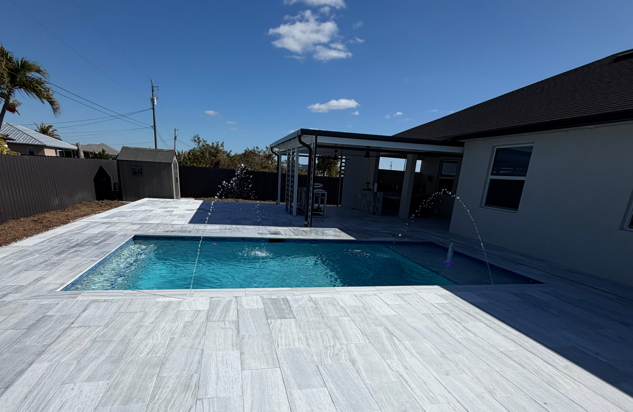 IMG_2083 1 Newly installed paver pool deck featuring a sparkling blue pool with water fountains, surrounded by a modern outdoor living space, showcasing Elite Pavers Solutions' quality craftsmanship in Southwest Florida.