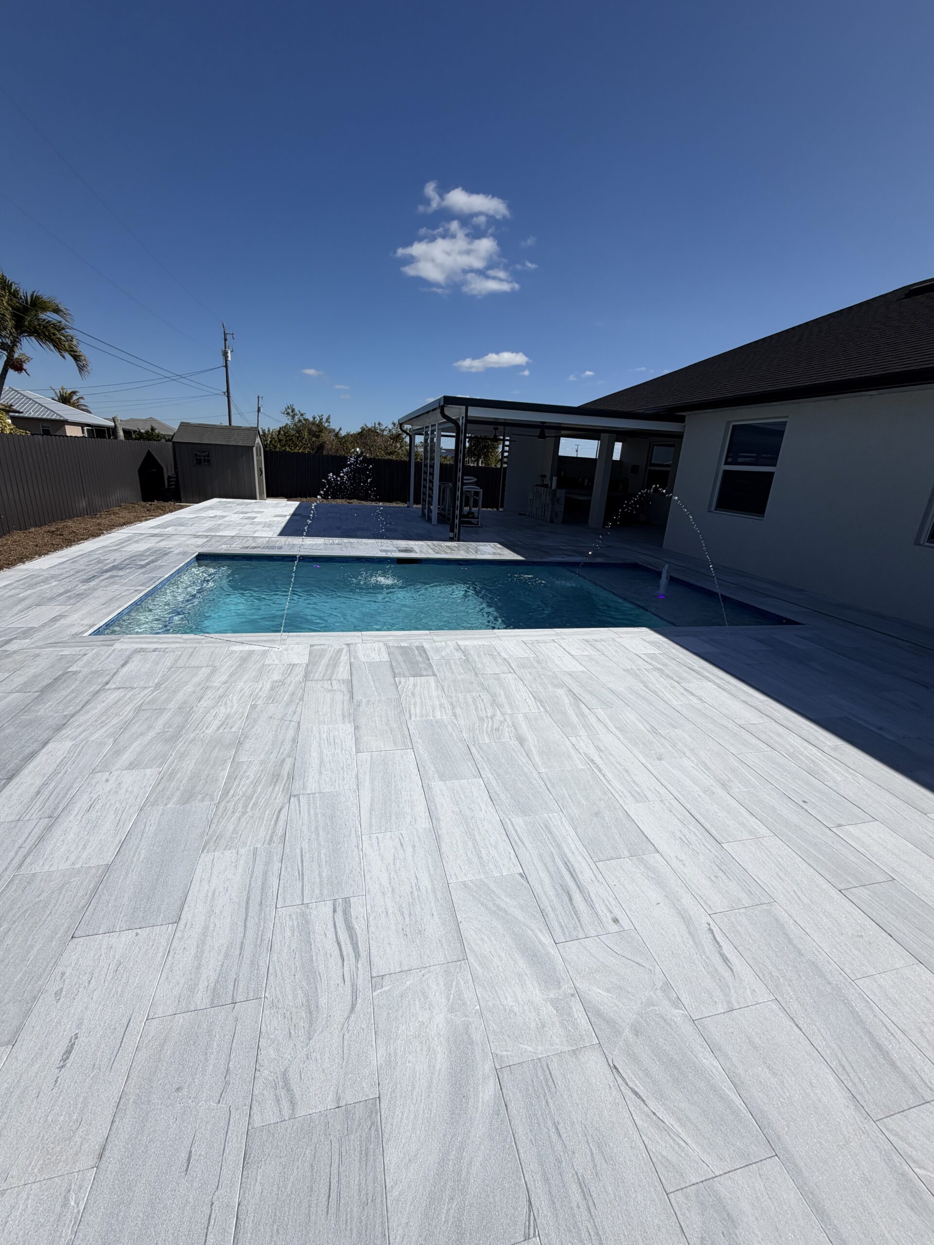 Paver installation showcasing gray stone tiles surrounding a swimming pool in a Southwest Florida backyard, enhancing outdoor living space and aesthetic appeal.