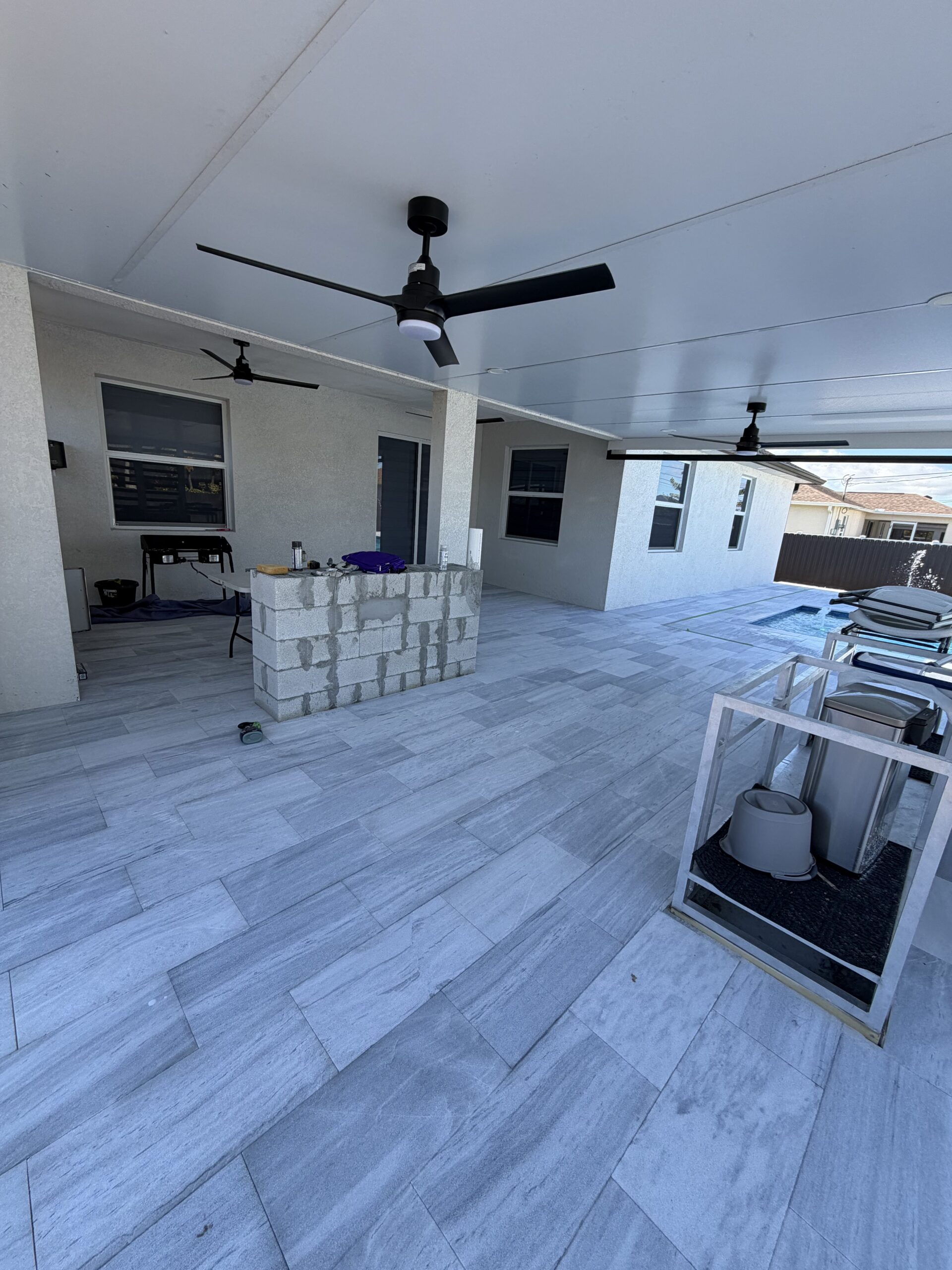 IMG_2084 Paver patio installation featuring large gray tiles, outdoor ceiling fans, and a construction area with block wall, showcasing Elite Pavers Solutions' craftsmanship in Southwest Florida.